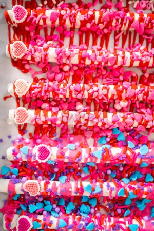 Photo for Drizzling melted chocolate over chocolate-dipped pretzels rods and decorating with sprinkles to make chocolate-covered pretzel rods for Valentines Day. - Royalty Free Image