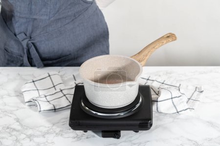 Téléchargez les photos : Chauffage crème fouettée dans une casserole pour faire le glaçage ganache chocolat blanc. - en image libre de droit
