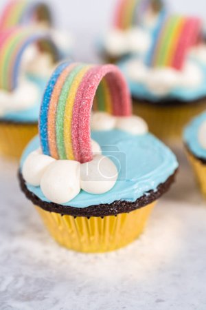 Foto de Pastelitos de chocolate decorados con glaseado de crema de mantequilla azul y arco iris para la fiesta de cumpleaños temática de unicornio. - Imagen libre de derechos