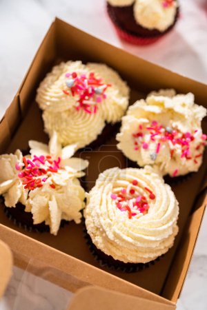 Photo for Packaging freshly baked red velvet cupcakes with white chocolate ganache frosting into the cupcake box. - Royalty Free Image