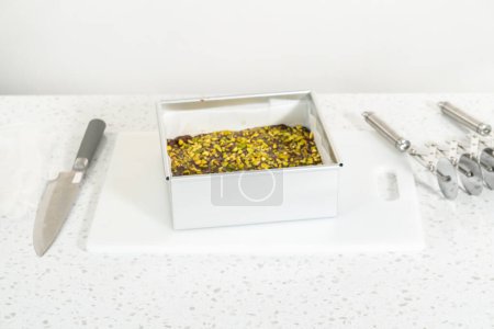 Foto de Removing chocolate pistachio fudge from a square cheesecake pan lined with parchment. - Imagen libre de derechos