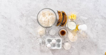 Téléchargez les photos : Ingrédients mesurés dans des bols en verre pour préparer des crêpes à la banane à la noix de coco pour le petit déjeuner. - en image libre de droit
