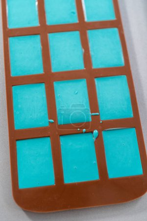 Foto de Rellenar moldes de silicona de chocolate con chocolate derretido para preparar mini barras de chocolate de sirena. - Imagen libre de derechos