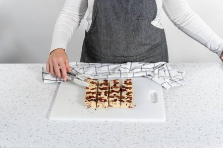 Photo for Cutting white chocolate cranberry pecan fudge into small pieces on a white cutting board. - Royalty Free Image