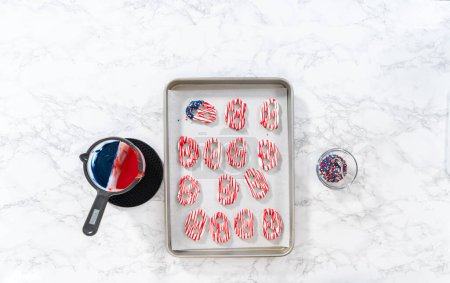 Flat lay. Dipping pretzels twists into melted chocolate to make red, white, and blue chocolate-covered pretzel twists.