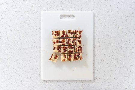 Photo for Flat lay. Cutting white chocolate cranberry pecan fudge into small pieces on a white cutting board. - Royalty Free Image
