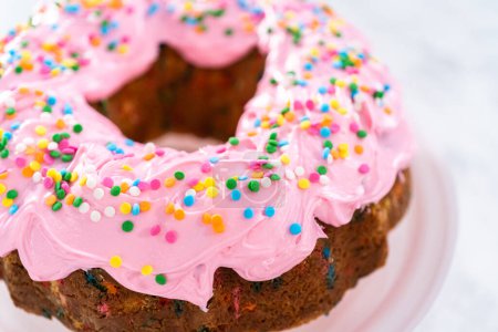 Téléchargez les photos : Gâteau bundt Funfettti givré à la crème au beurre à la vanille rose et décoré de saupoudres arc-en-ciel. - en image libre de droit