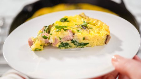 Photo for Step by step. Slicing freshly baked spinach and ham frittata in cast iron skillet. - Royalty Free Image