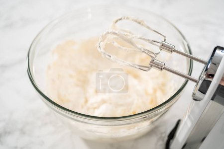Photo for Whisking buttercream frosting in a glass mixing bowl with an electric hand mixer to prepare the peppermint buttercream frosting. - Royalty Free Image