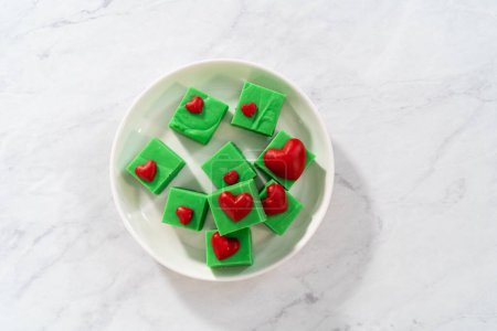 Photo for Homemade chocolate green fudge with red hearts square pieces on a white plate. - Royalty Free Image