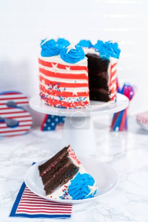 Téléchargez les photos : Trancher le gâteau au chocolat du 4 juillet décoré de glaçage à la crème au beurre rouge, blanc et bleu. - en image libre de droit