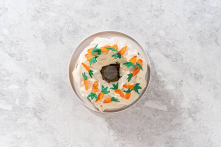 Photo for Flat lay. Decorating freshly baked carrot bundt cake with cream cheese frosting with chocolate carrot cake toppers. - Royalty Free Image