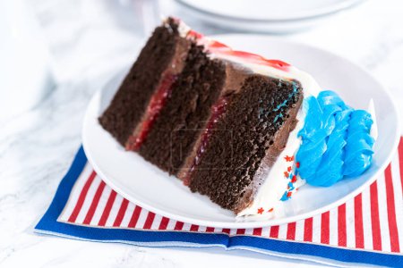 Foto de Rebanada de pastel de chocolate del 4 de julio decorado con glaseado de crema de mantequilla roja, blanca y azul en un plato blanco. - Imagen libre de derechos