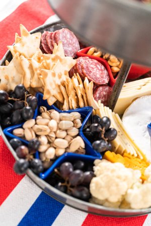 Photo for July 4th charcuterie board on a two-tiered serving metal stand filled with cheese, crackers, salami, and fresh fruits - Royalty Free Image
