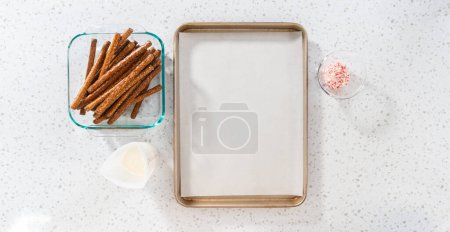 Téléchargez les photos : Pose plate. Tremper les tiges de bretzel dans du chocolat fondu et saupoudrer de bonbons de canne à sucre écrasés pour faire des tiges de bretzel recouvertes de chocolat de canne à sucre. - en image libre de droit