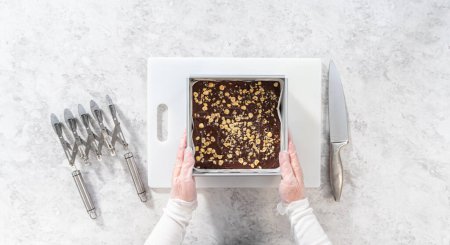 Téléchargez les photos : Pose plate. Enlever le caramel au chocolat noisette d'un moule à gâteau au fromage carré doublé de parchemin. - en image libre de droit
