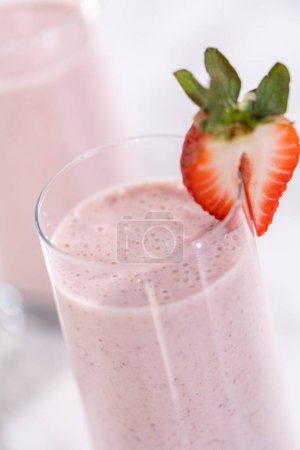 Photo for Freshly made healthy breakfast strawberry banana smoothie garnished with fresh strawberry and paper straw. - Royalty Free Image