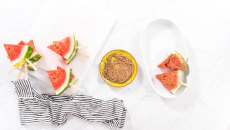 Photo for Flat lay. Dipping watermelon pops into the chili lime salt to prepare Mexican watermelon pops. - Royalty Free Image