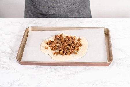 Téléchargez les photos : Préparation de pizza dessert à la cannelle sur une plaque à pâtisserie tapissée de papier parchemin. - en image libre de droit