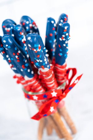 Foto de Barras de pretzel cubiertas de chocolate caseras decoradas como la bandera estadounidense en un frasco de vidrio. - Imagen libre de derechos