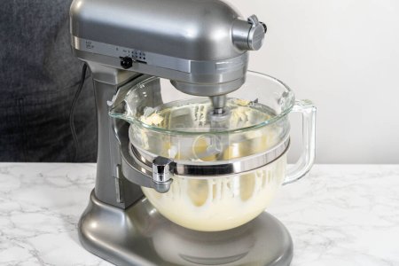 Téléchargez les photos : Whisking buttercream frosting in a glass mixing bowl with an electric kitchen mixer for American flag mini cupcakes. - en image libre de droit