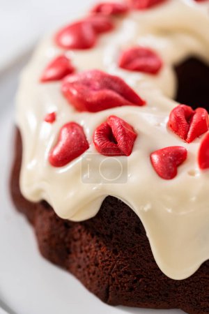 Téléchargez les photos : Freshly baked red velvet bundt cake with chocolate lips and hearts over cream cheese glaze for Valentines Day. - en image libre de droit