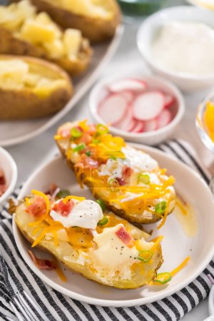 Téléchargez les photos : Pressure Cooker Baked Potatoes. Garnished large baked potatoes with butter, sour cream, cheese, and bacon bits on a white plate. - en image libre de droit