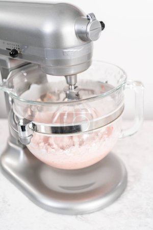 Foto de Batiendo crema de mantequilla de fresa glaseado en una batidora eléctrica independiente con un accesorio de batidor. - Imagen libre de derechos