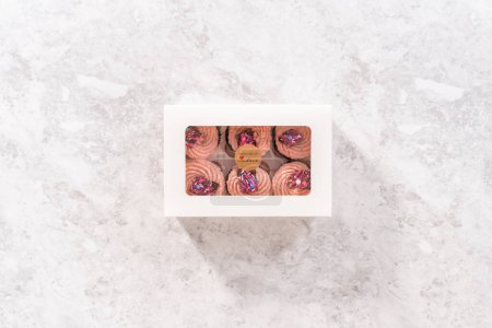 Téléchargez les photos : Pose plate. Emballage de cupcakes fraises au chocolat fraîchement cuits garnis de mini chocolats roses gourmands dans une boîte à cupcakes en papier blanc. - en image libre de droit