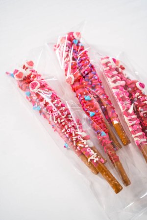 Chocolate-covered pretzel rods decorated with heart-shaped sprinkles for Valentines Day packaged in a clear bags.