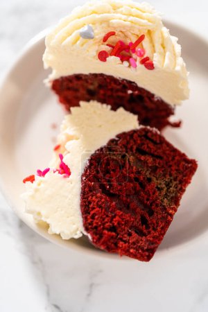 Téléchargez les photos : Cupcakes en velours rouge tranchés avec glaçage ganache au chocolat blanc sur une assiette blanche. - en image libre de droit