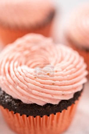 Foto de Cupcakes de chocolate esmerilados con glaseado de crema de mantequilla de fresa. - Imagen libre de derechos