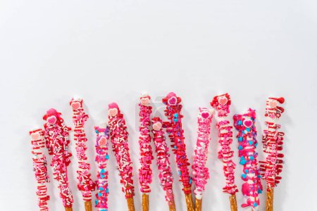 Photo for Flat lay. Chocolate-covered pretzel rods decorated with heart-shaped sprinkles for Valentines Day. - Royalty Free Image