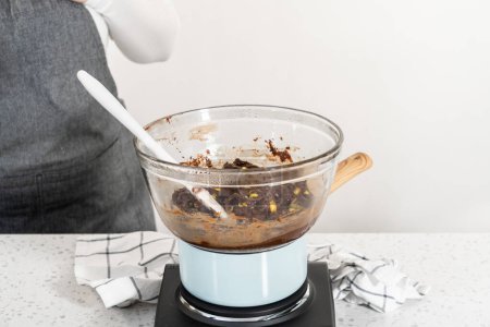 Téléchargez les photos : Melting white chocolate chips and other ingredients in the double boiler to prepare chocolate pistachio fudge. - en image libre de droit