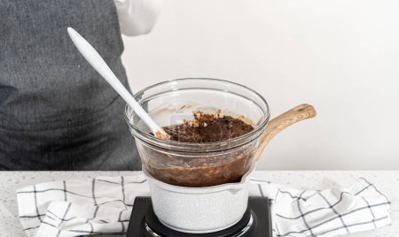 Téléchargez les photos : Faire fondre les pépites de chocolat et d'autres ingrédients dans un bol de mélange en verre sur de l'eau bouillante pour préparer du caramel nature. - en image libre de droit