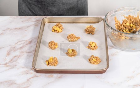 Téléchargez les photos : Enfoncer la pâte à biscuits dans la plaque à pâtisserie tapissée de papier parchemin pour faire cuire les biscuits à l'avoine de pomme. - en image libre de droit