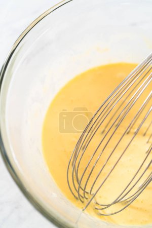 Foto de Mezclar ingredientes húmedos en un tazón de vidrio grande para hornear pastel de paquete de arándanos limón. - Imagen libre de derechos