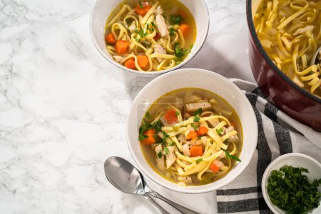 Photo for Serving chicken noodle soup with kluski noodles in white ceramic soup bowls. - Royalty Free Image