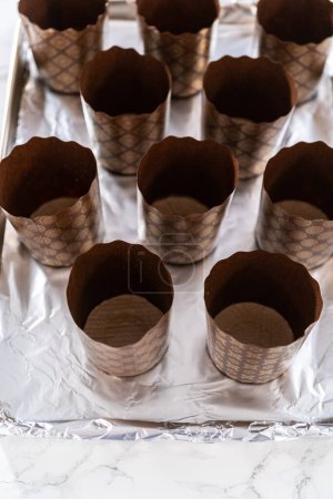Foto de Recoger masa de pan en revestimientos de papel para hornear mini kulich de pan de Pascua. - Imagen libre de derechos