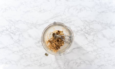 Photo for Flat lay. Scooping cookie dough with dough scoop into a baking sheet lined with parchment paper to bake soft oatmeal raisin walnut cookies. - Royalty Free Image
