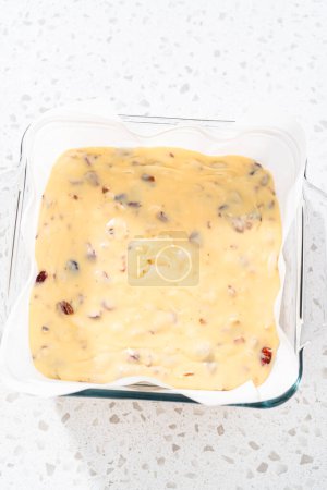 Photo for Pouring fudge mixture into the baking pan lined with parchment paper to prepare white chocolate cranberry pecan fudge. - Royalty Free Image