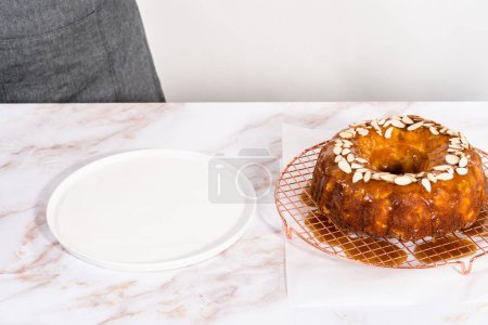 Photo for Glazing homemade caramel glaze over freshly baked apple bundt cake and garnishing with sliced almonds. - Royalty Free Image