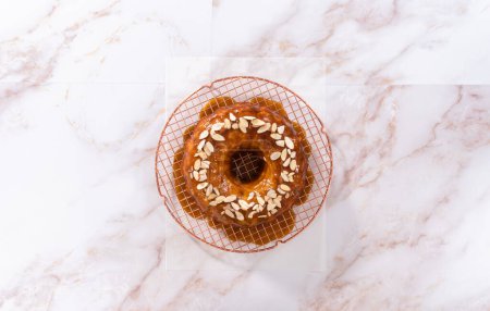 Photo for Flat lay. Glazing homemade caramel glaze over freshly baked apple bundt cake and garnishing with sliced almonds. - Royalty Free Image