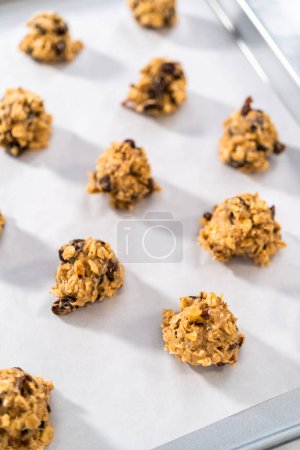 Téléchargez les photos : Ramasser la pâte à biscuits avec une cuillère à pâtisserie dans une plaque à pâtisserie doublée de papier parchemin pour faire cuire des biscuits aux noix de raisin à l'avoine molle. - en image libre de droit
