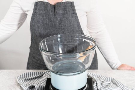 Foto de Derretir chispas de chocolate y otros ingredientes en un tazón de vidrio sobre agua hirviendo para preparar caramelos de maíz dulce. - Imagen libre de derechos