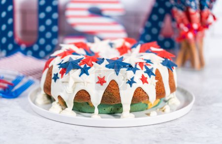 Téléchargez les photos : 4 juillet gâteau bundt recouvert d'une glaçure vanille et décoré avec des étoiles de chocolat sur une assiette blanche. - en image libre de droit