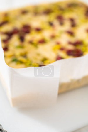 Téléchargez les photos : Enlever le caramel à la pistache aux canneberges d'une poêle à gâteau au fromage carrée doublée de parchemin. - en image libre de droit