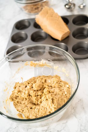 Téléchargez les photos : Ramasser la pâte avec une cuillère à pâtisserie dans une casserole à cupcake doublée de doublures de muffins en papier tulipe pour cuire des muffins à l'avoine banane. - en image libre de droit