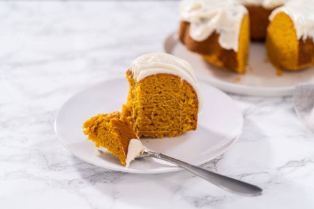 Slice of homemade pumpkin bunt cake with cream cheese frosting on a white plate.
