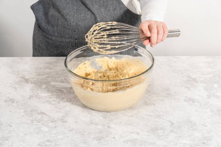 Photo for Mixing wet and dry ingredients with a hand whisk in a glass mixing bowl to bake a carrot bundt cake with cream cheese frosting. - Royalty Free Image